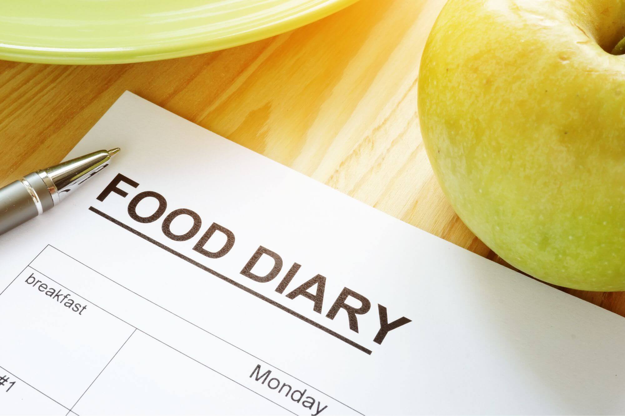 Photo of a food diary and pen next to a healthy apple
